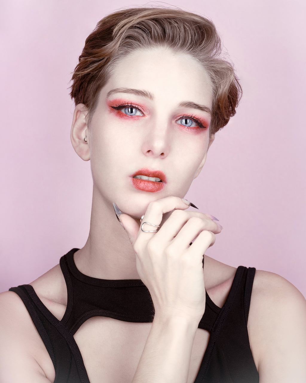 Rosée d’agrumes III par SchaPicShow : portrait sur fond rose poudré, une main sous le menton, regard direct et maquillage corail.